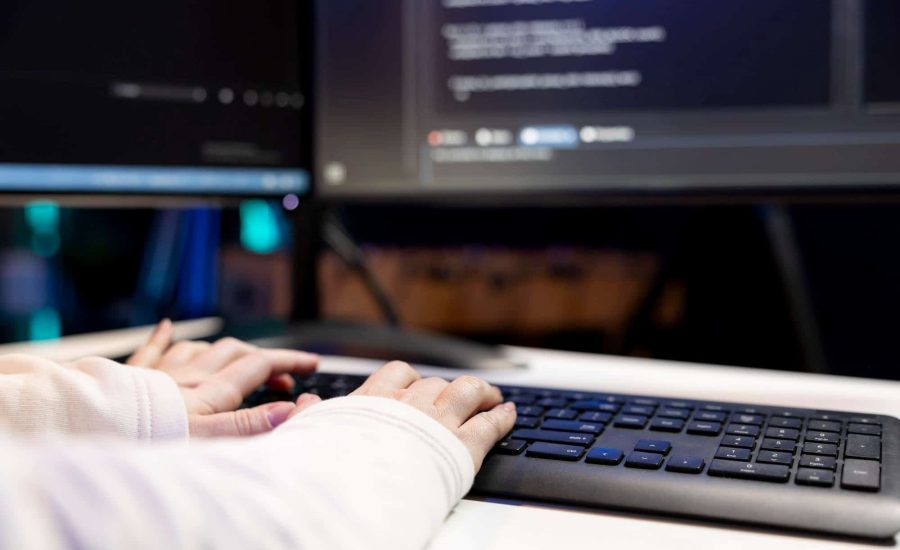 Fotografía de manos escribiendo en teclado con código en pantalla representando el servicio de mantenimiento y desarrollo web de Adrián García